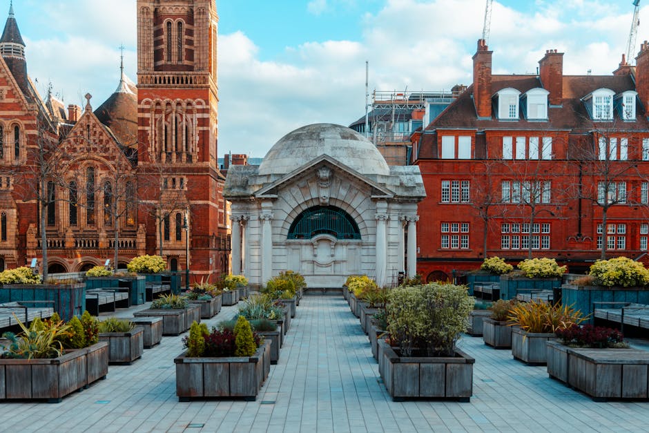 A rooftop garden with neatly arranged rectangular wooden planter boxes filled with various plants, including small shrubs, perennial flowers, and ornamental grasses. The garden features paved walkways
